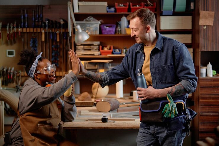 Two men sharing a high-five in a woodworking workshop.